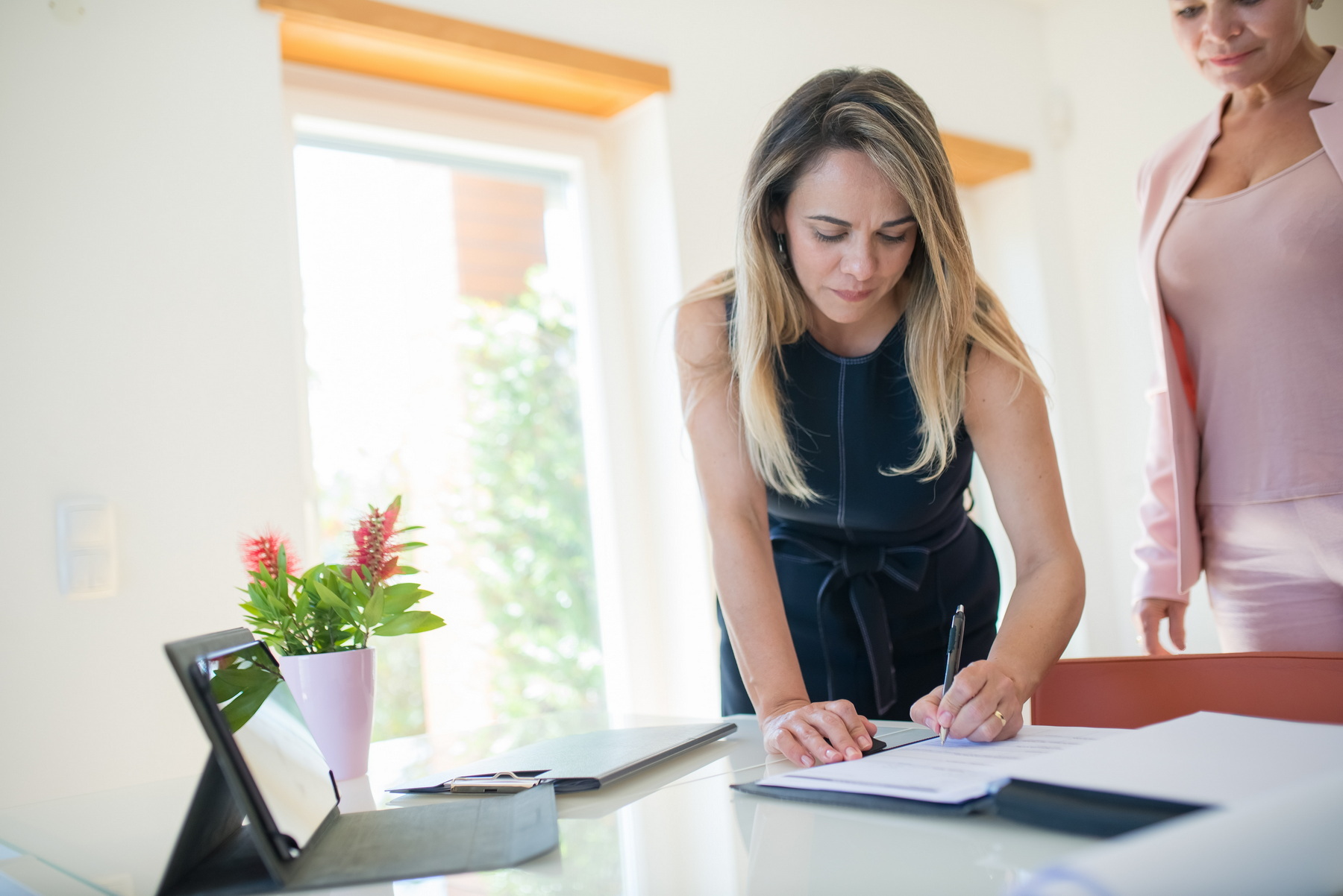 Two women signing a document. The documents could be an Apostille, Affidavits, or Certified True Copies